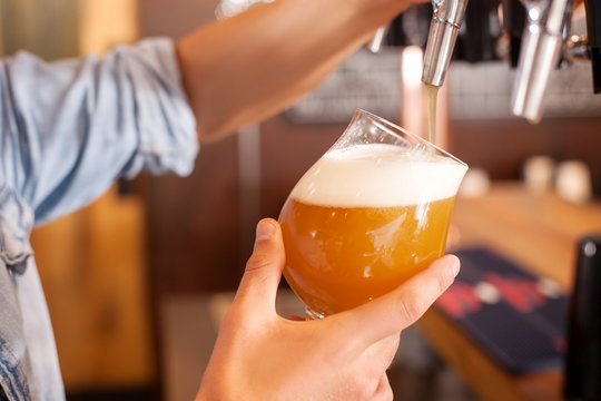 Cheerful young bartender is pouring lager in pub