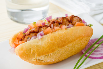 A spicy gourmet style hot dog with tomato, onion and basil