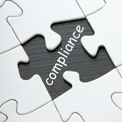 The word compliance in white text on a blackboard as revealed by a missing jigsaw puzzle piece