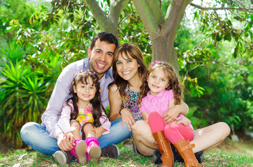 Fototapeta na wymiar Beautiful hispanic family of four sitting outside on grass