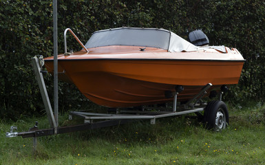 A boat on a trailer in front of a hedge
