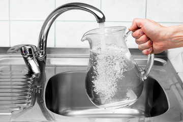 Pitcher being filled with drinking water from kitchen faucet. - obrazy, fototapety, plakaty