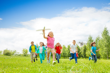 Small girl holding airplane toy and kids behind