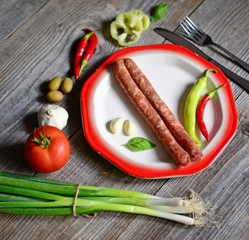 Portion of sausages on plate with tomatoe, fresh onion, chilly p