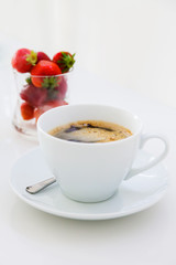 A cup of black coffee and strawberries on a white table