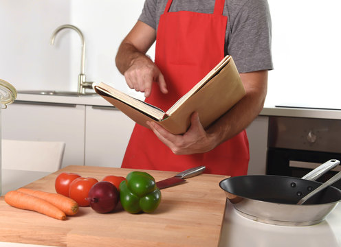 unrecognizable man in apron at kitchen following recipe book healthy cooking