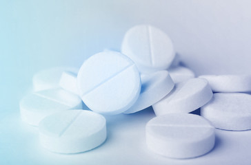 Close up of a heap of white medicine pills on white surface.
