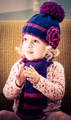 Portrait of cheerful girl clapping with a knitted cap and scarf sitting on a chair in a retro style.