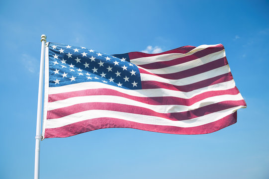 The red, white, and blue stars and stripes of an American flag waving in bright blue sky