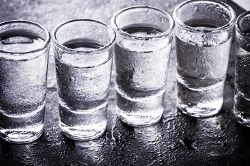 Vodka shot glass on wet black surface.