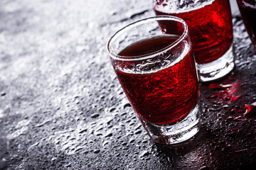 Red vodka shots on wet black surface.