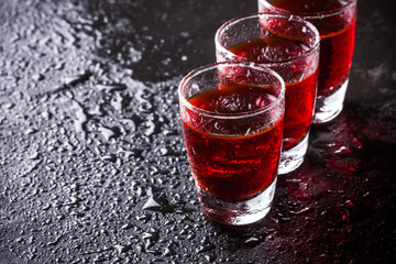 Red vodka shots on wet black surface.