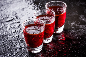 Red vodka shots on wet black surface.