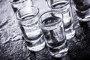 Vodka shot glass on black wet surface.