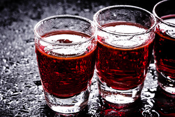 Red vodka shots on wet black surface.
