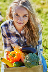Young woman holding wooden crate with vegetables