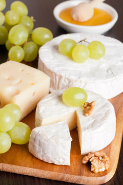 cheeses, honey, grapes and walnuts on a wooden background