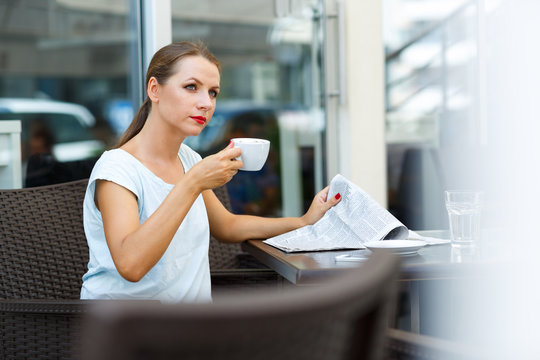 Attractive woman reading a newspaper and drinking morning coffee
