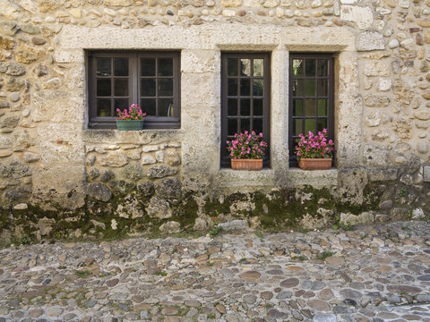 Windows of an old stone house at medieval village Perouge in France with flower pots