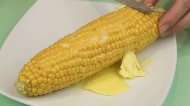 Spreading butter on a hot cob of corn straight from the oven