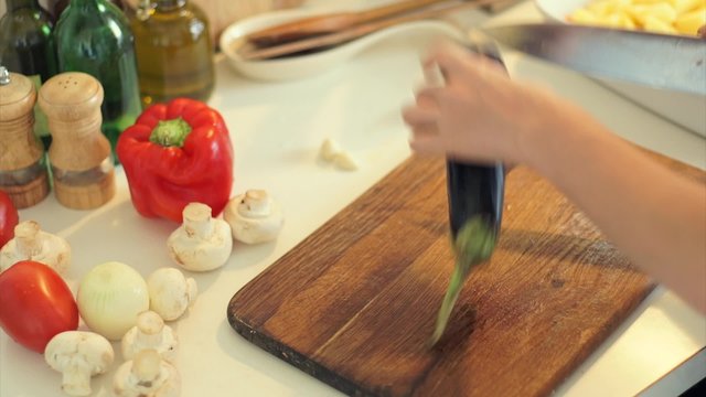 Female hands slicing eggplant vegetables on kitchen board close up