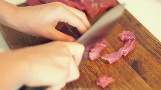 Female hands slicing meat on kitchen board close up