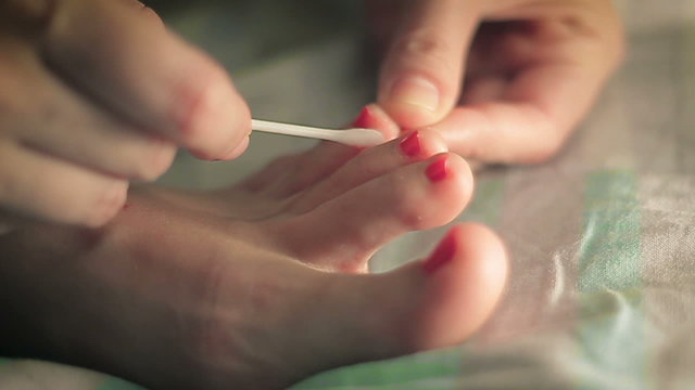 Woman paints her toenails red lacquer