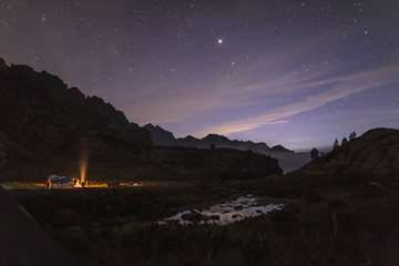 Tourists and hunters are heated around the campfire at night in the mountains in the background of...