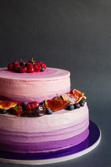 Two tiered purple cake with fruit on dark gray background