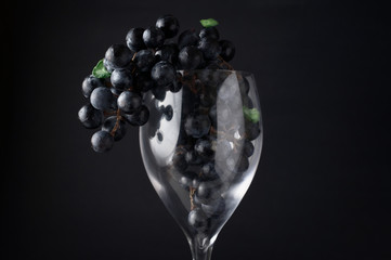 Grapes in red wine glass hanging over against dark background