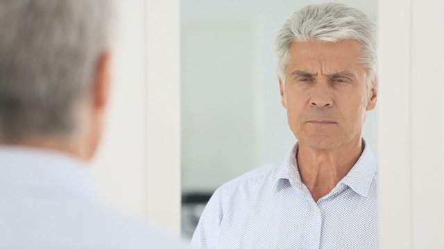 Senior man trying eyglasses on in front of mirror