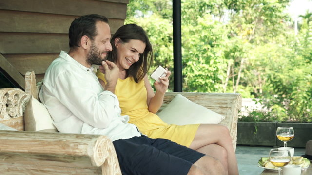 Happy couple watching movie on smartphone sitting on terrace
