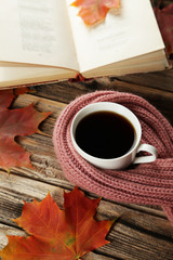 Cup of coffee with autumn leaves and a warm scarf on brown wooden background