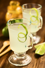 Hot lemonade made of fresh limes and brown sugar served in glass and garnished with lime peel on dark wood (Selective Focus, Focus on the front of the glass rim and on the peel)