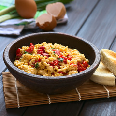 Scrambled eggs made with red bell pepper and green onion in rustic bowl, photographed with natural light (Selective Focus, Focus one third into the eggs)