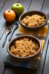 Baked apple crumble or crisp, photographed on dark wood with natural light (Selective Focus, Focus one third into the first crumble)
