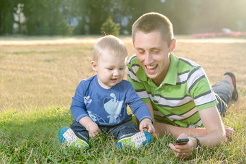 Fototapeta na wymiar cheerful young father with his young son using a mobile phone