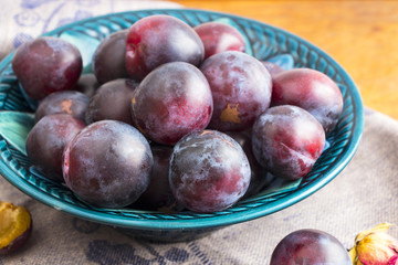 Purple plums in a green plate on a wooden table
