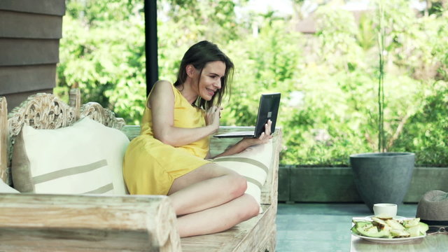 Pretty, young woman using laptop lying on sofa on terrace
