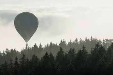 Obraz premium Hot air balloon above the foggy forest