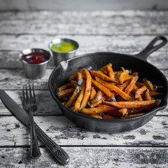 Sweet potato fries in cast iron skillet on wooden background