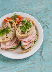 sandwich with whole grain bread, cucumber and ham on a white plate on blue wooden surface