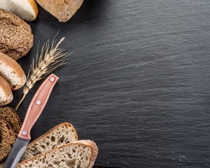 Bread slices, a wheat and a knife on the black stone desk.