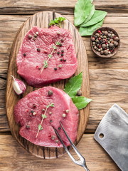 Raw beaf steaks with spices on a wooden board.