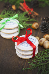 Christmas cookies with ribbons, apples, nuts, cones, cinnamon and green arborvitae branch on a wooden table.