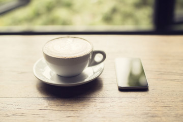 Smartphone and cup of cappuccino on a wooden table