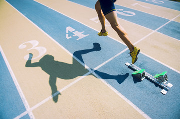 Athlete in gold shoes sprinting from the starting blocks over the starting line of a race on a blue...