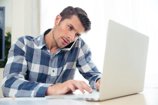 Man Paying His Bills With Laptop While Talking On Phone