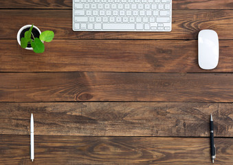 Brown Wooden Desk with Stationery and Electronics Natural Wood Background Small Green Plant Computer Mouse and Keyboard Black and White Pens Top View