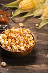 Wooden bowl full of sweet caramel popcorn with caramel sauce and corncobs over rustic table. Vintage style. Selective focus